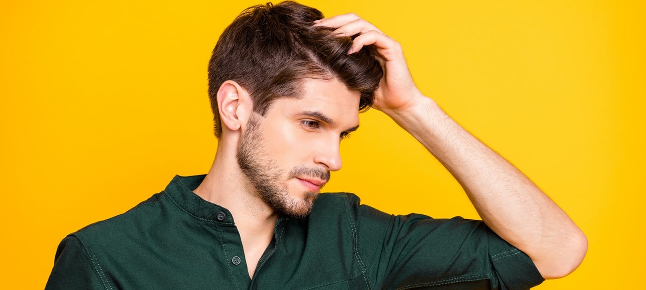  Ein seri&ouml;ser Mann ber&uuml;hrt sein Haar, um den Haarausfall zu &uuml;berpr&uuml;fen.