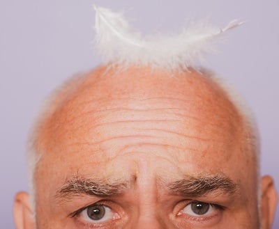 Ein &auml;lterer Mann mit einer Feder auf dem kahlen Kopf als ein Symbol f&uuml;r Haarausfall im Alter.