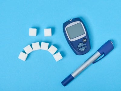 : Ein trauriges Emoticon aus Zuckerst&uuml;cken neben einem Blutzuckermessger&auml;t