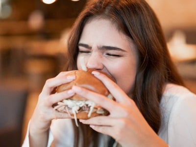  Eine junge Frau isst einen Burger, weil sie einen Hei&szlig;hungeranfall hat